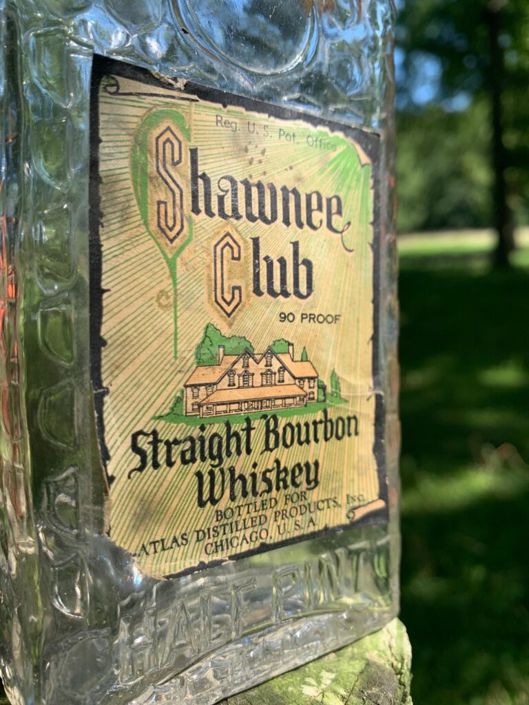 Close-up of an old Shawnee Club Straight Bourbon Whiskey bottle with vintage label, featuring 90 proof and an image of a house